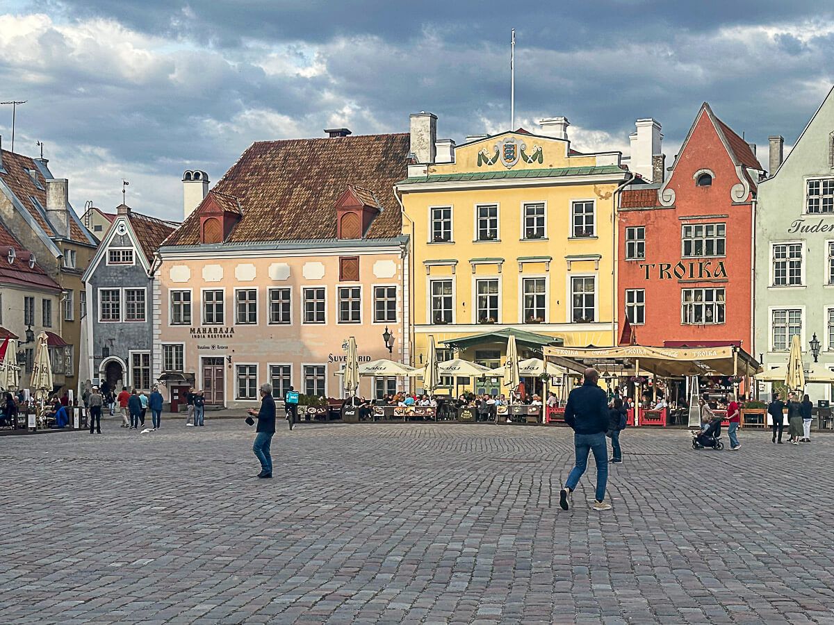 Altstadtplatz mit bunten Häusern. Davor Lokale und spazierende Menschen