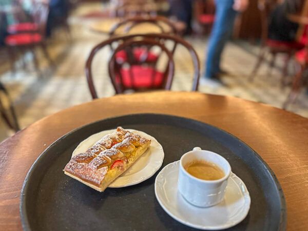 Kaffeehaus mit Tischen und Stühlen und im Vordergrund Kaffee und Kuchen auf einem Tisch