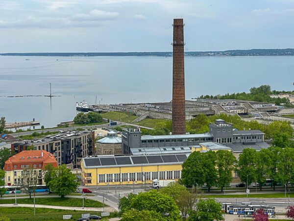 Blick auf einen Fabrikschornstein, dahinter ein Lost Place und das Meer
