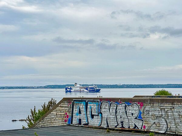 Mauer der Linnahll mit Mural, dahinter eine Fähre, die in den Hafen einläuft